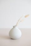 Ceramic round bud vase in white with natural specs from the side view holding a few dried florals.