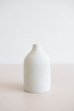 Ceramic bud vase with narrow mouth in white with natural specs from the side view.