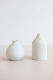 A pair of ceramic bud vases comparing a round shape and a taller narrow shape from the side view.