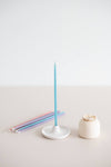 Giving set that includes a pack of pastel beeswax candles, a handmade ceramic candle holder and match striker. Blue candle in candle holder.
